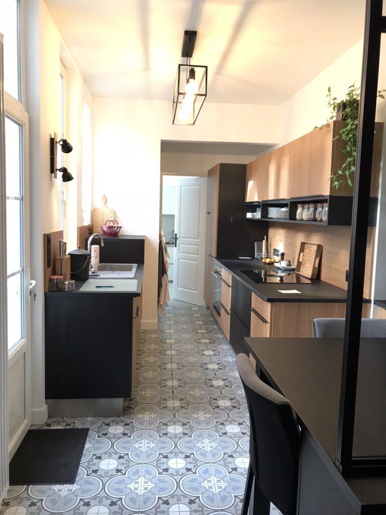 Cuisine moderne rénovée avec meubles noir et bois, plan de travail sombre et carrelage style carreaux de ciment.