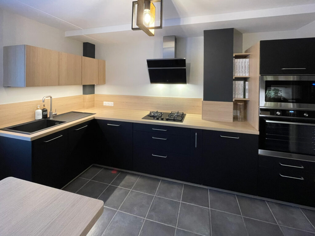 Cuisine moderne noire avec plan de travail effet bois et crédence assortie après rénovation de la cuisine.