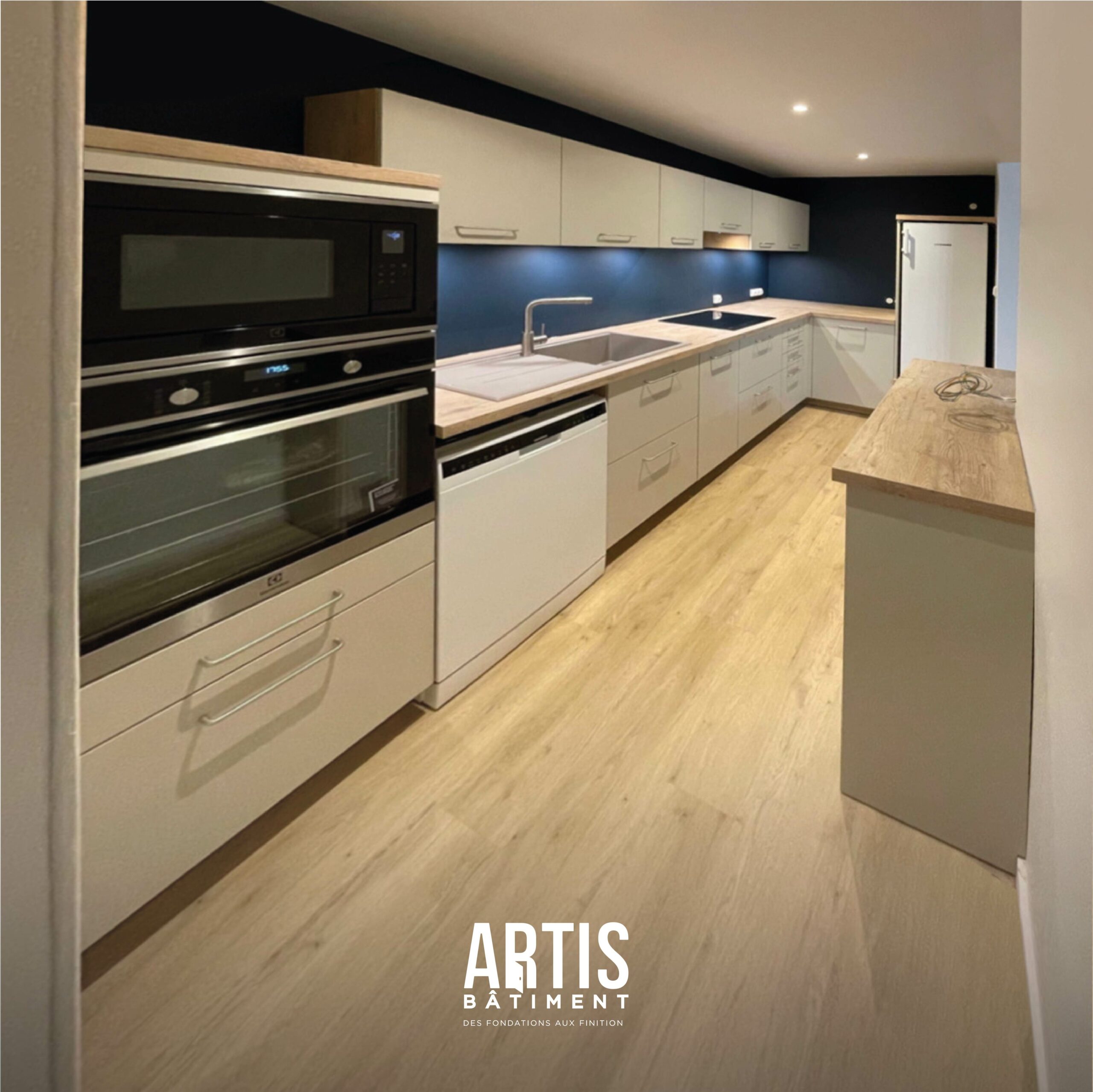 Cuisine moderne blanche avec plan de travail effet bois et électroménager intégré après rénovation.