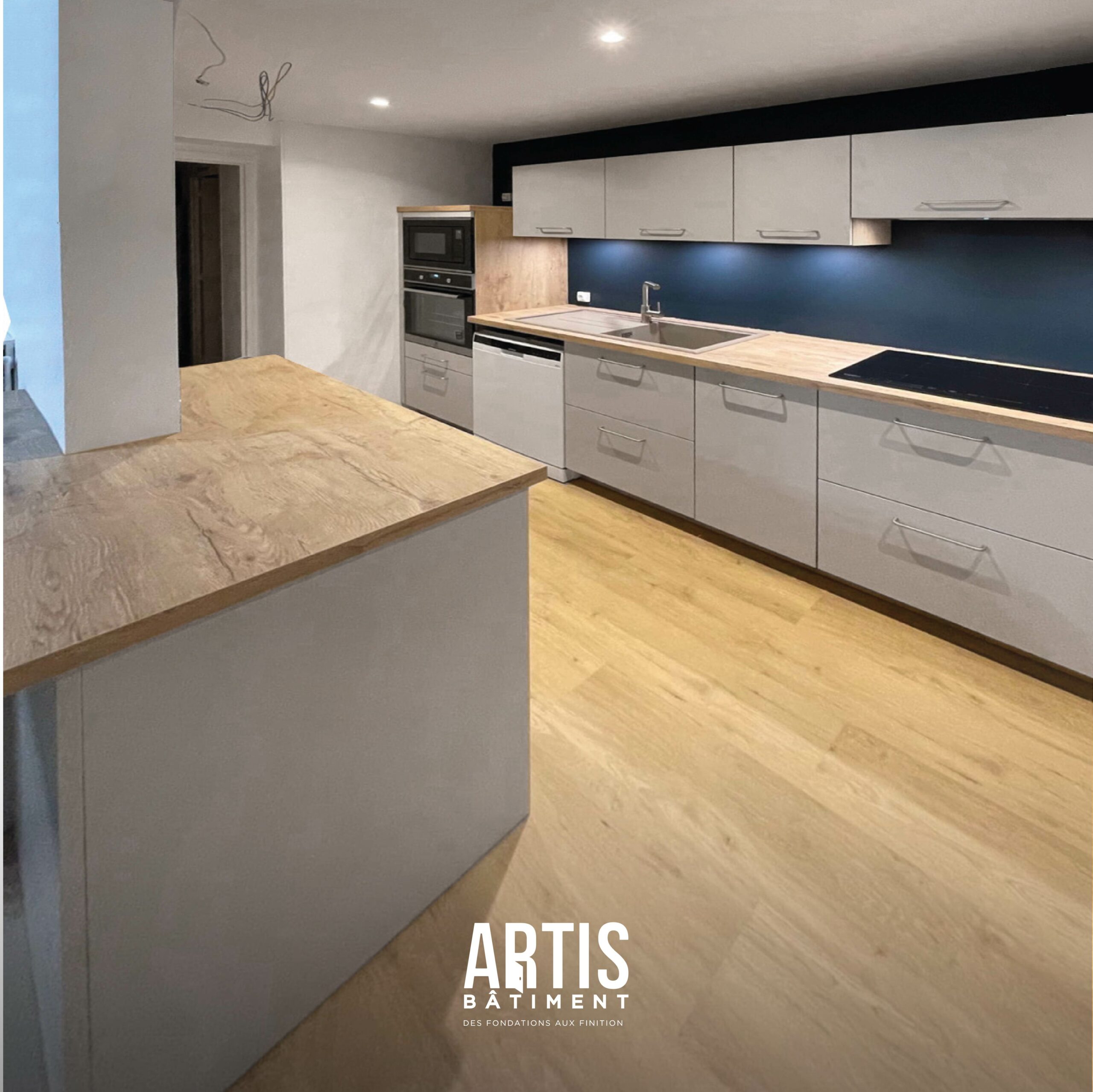 Cuisine moderne rénovée avec îlot central, façades blanches et plan de travail effet bois.