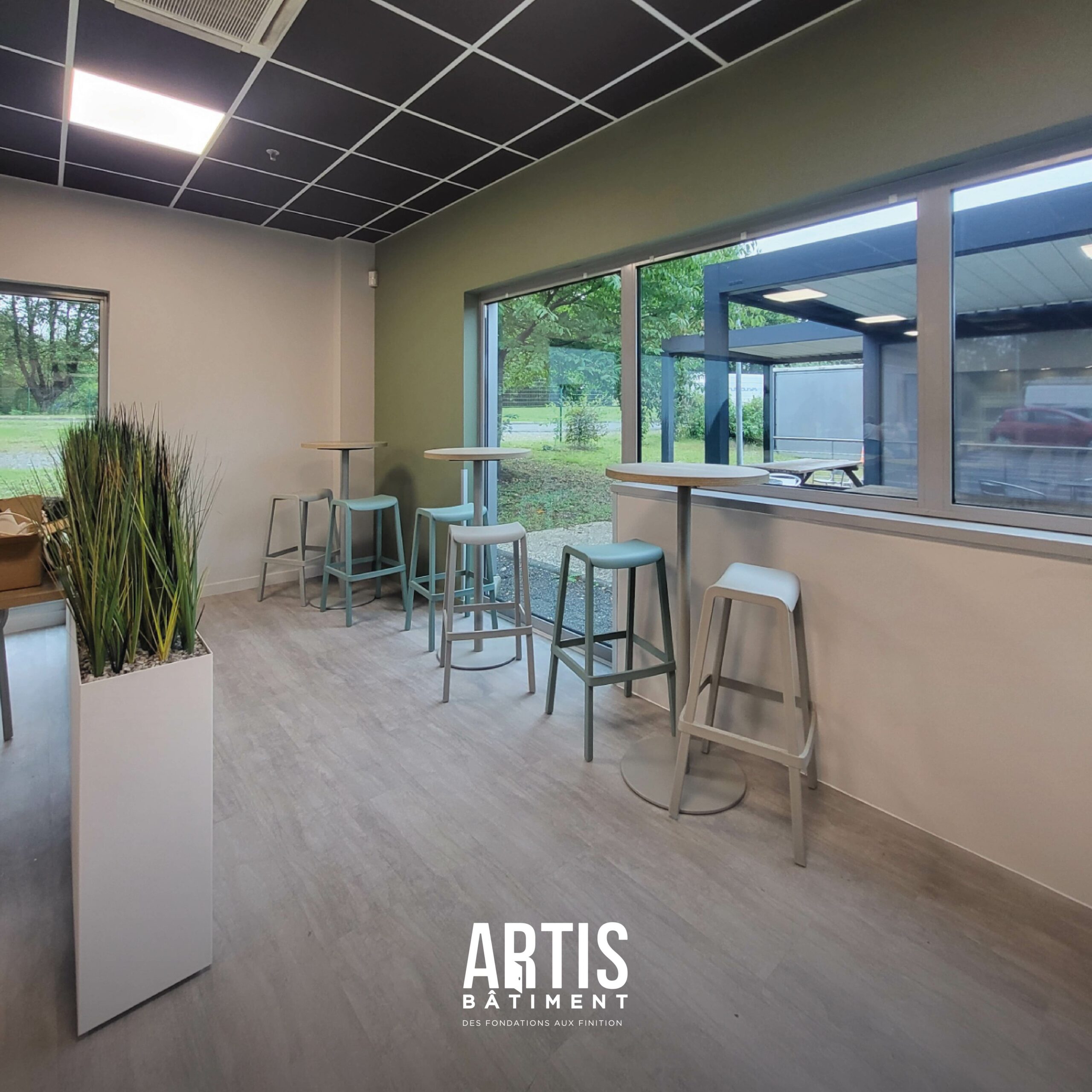 Espace repas dans une salle de pause d’entreprise avec tables hautes près des fenêtres.