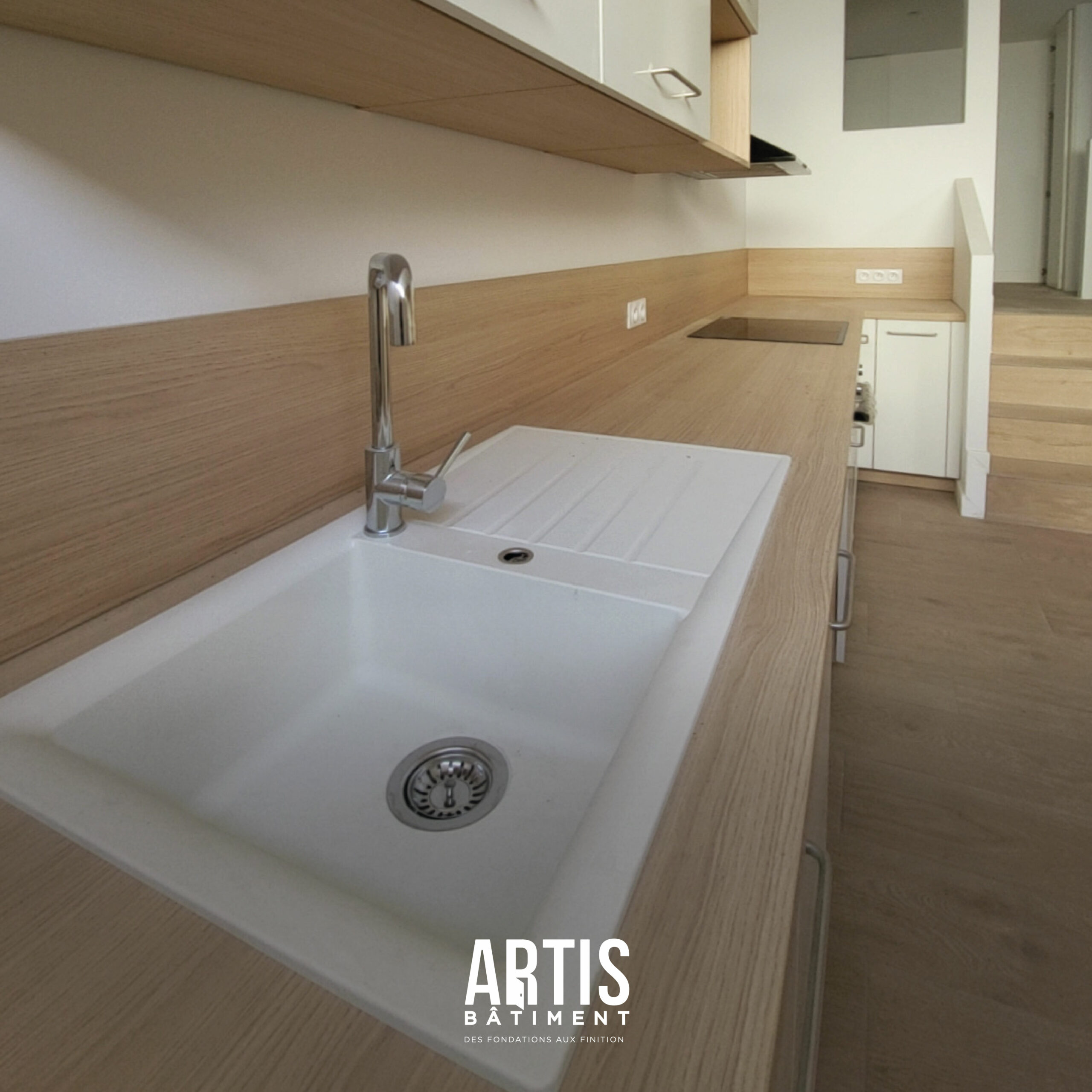 Cuisine rénovée avec plan de travail bois, évier blanc et crédence assortie.