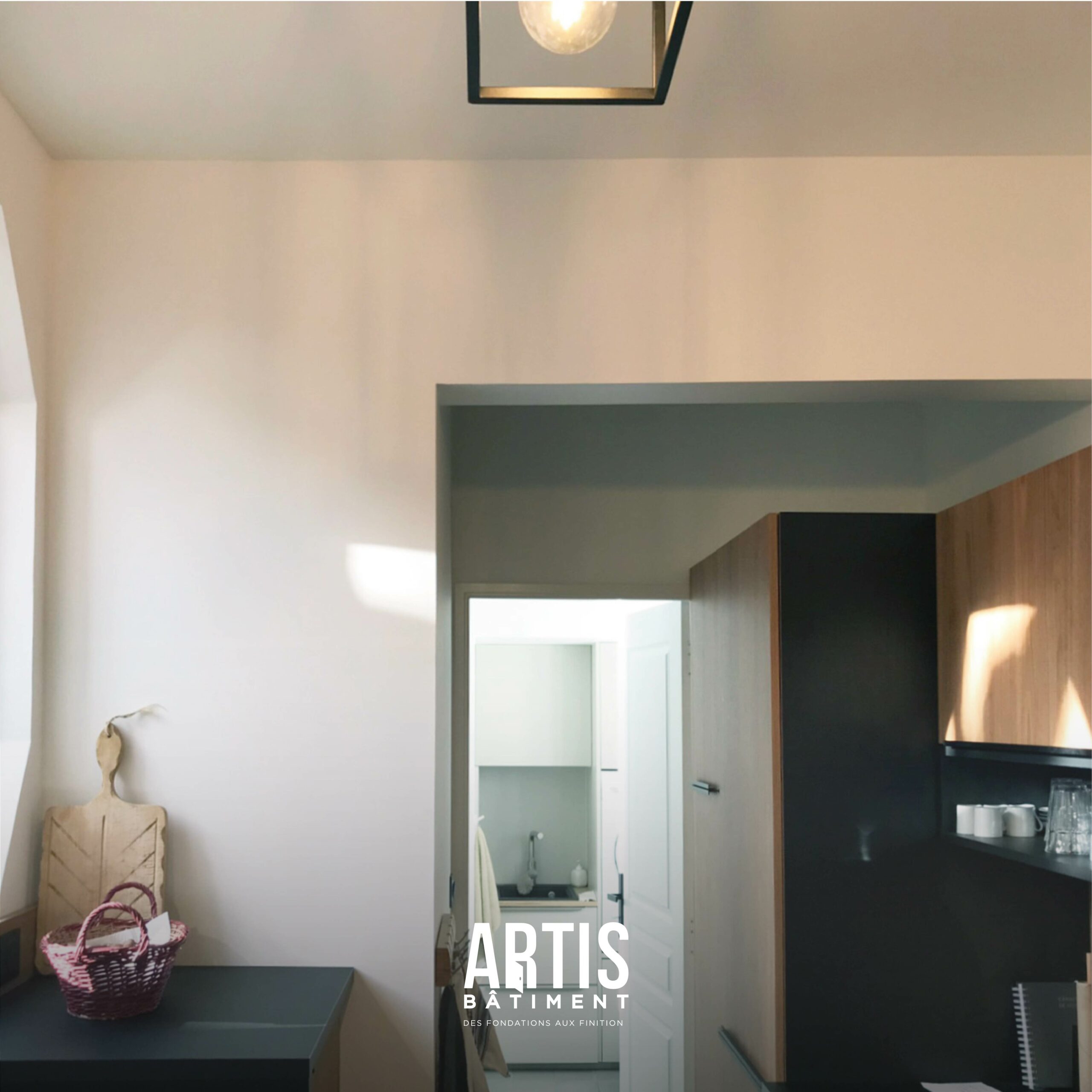 Cuisine rénovée moderne avec rangements bois, plan de travail noir et éclairage suspendu.