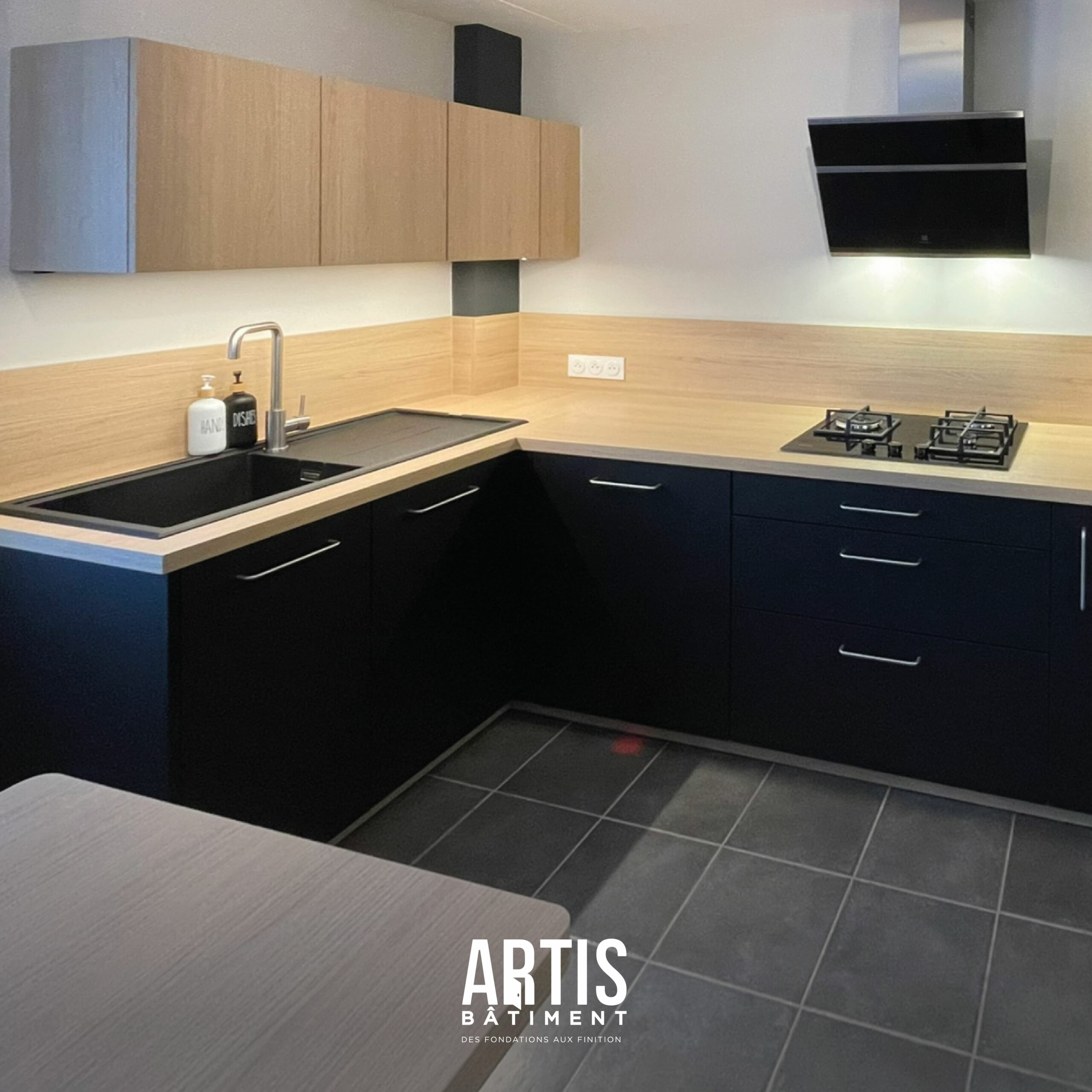 Cuisine moderne noire avec plan de travail effet bois et crédence assortie après rénovation de la cuisine.
