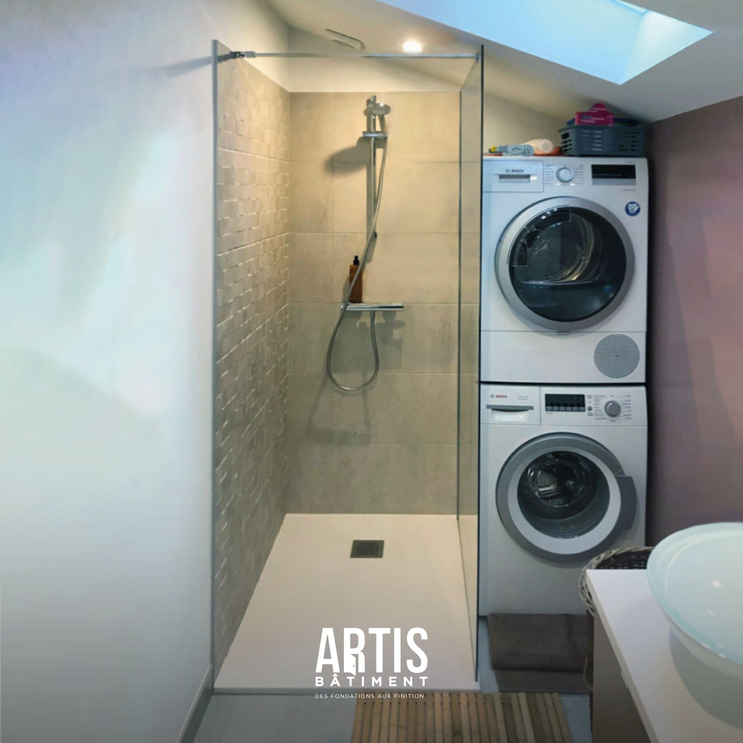 Salle de bain rénovée avec douche à l’italienne, paroi vitrée et carrelage beige.