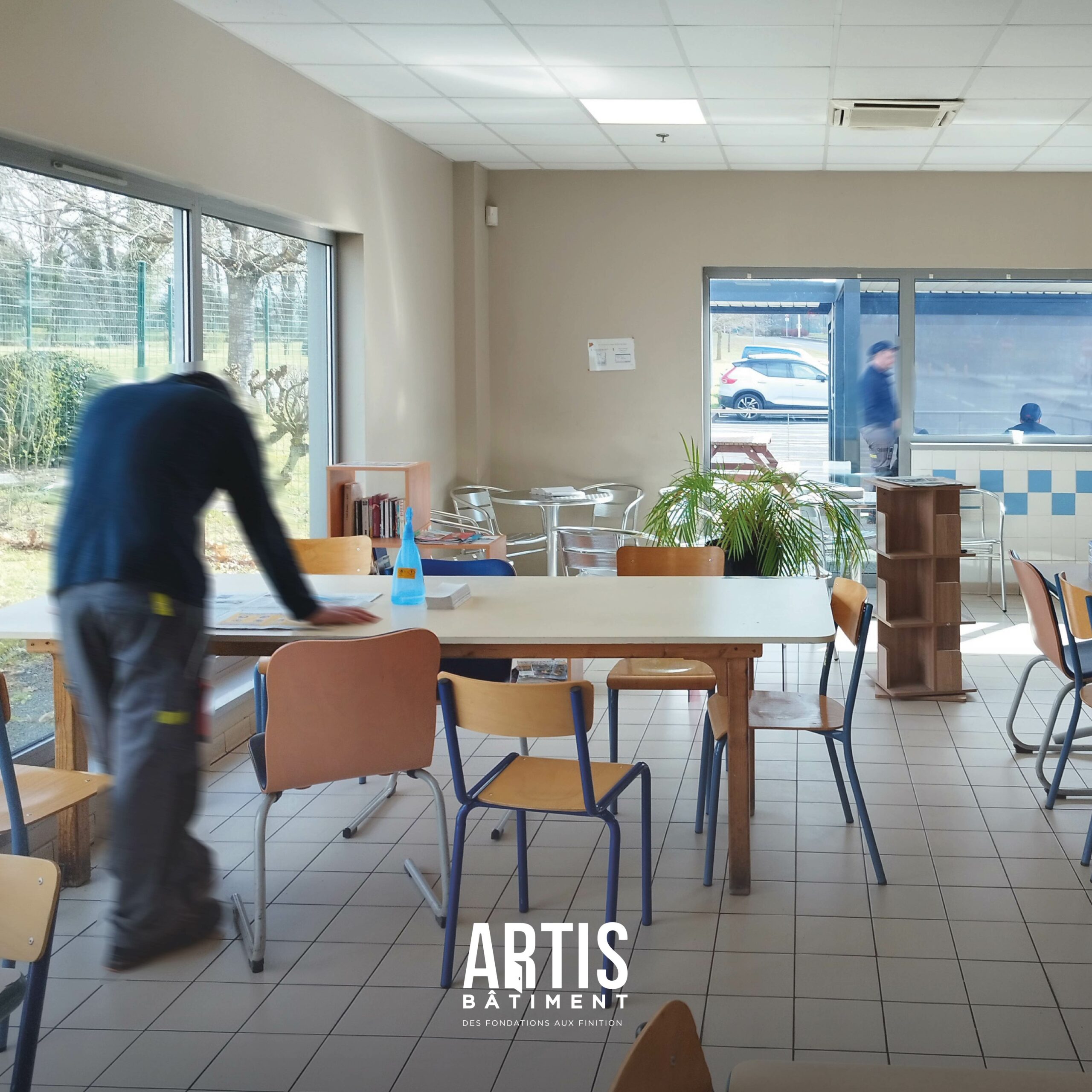 Salle de pause d’entreprise avec grandes fenêtres et tables avant rénovation.