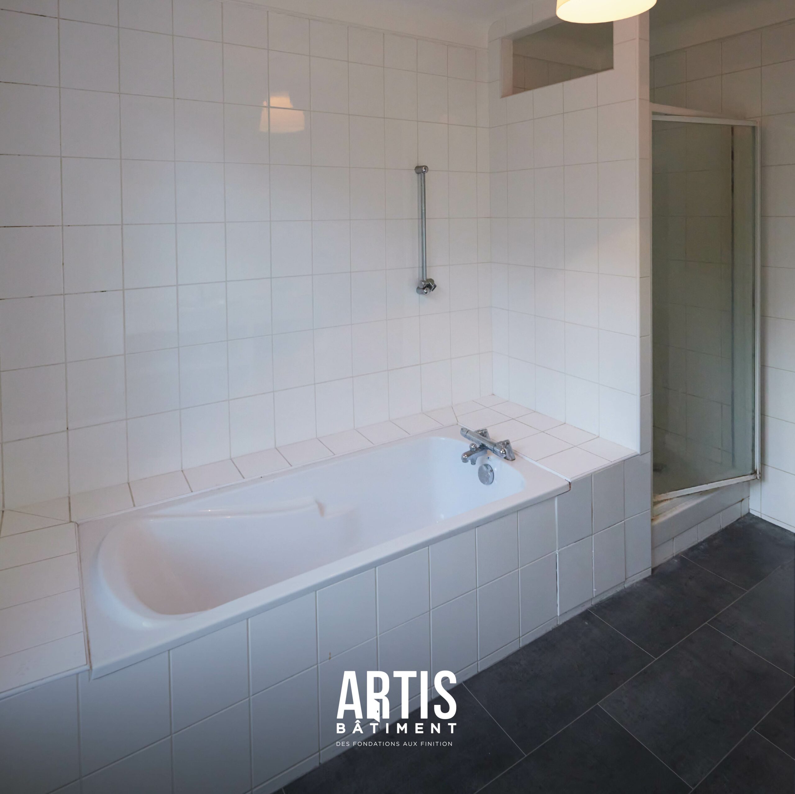 Ancienne salle de bain avec baignoire et carrelage blanc avant rénovation complète.