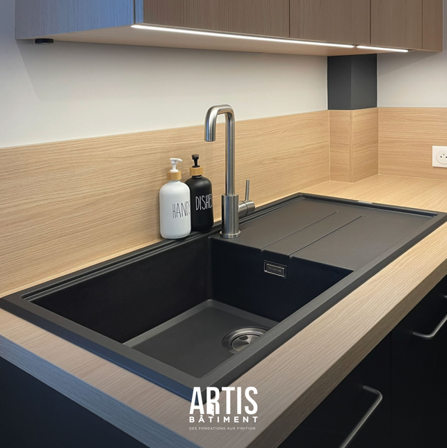 Évier noir avec mitigeur inox intégré dans une cuisine moderne avec plan de travail effet bois.