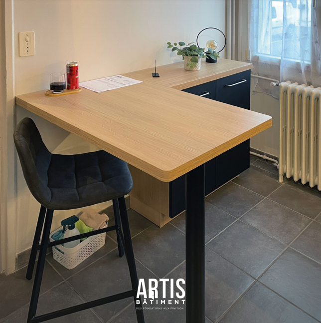 Coin repas intégré à la cuisine avec plan de travail effet bois et tabouret noir.