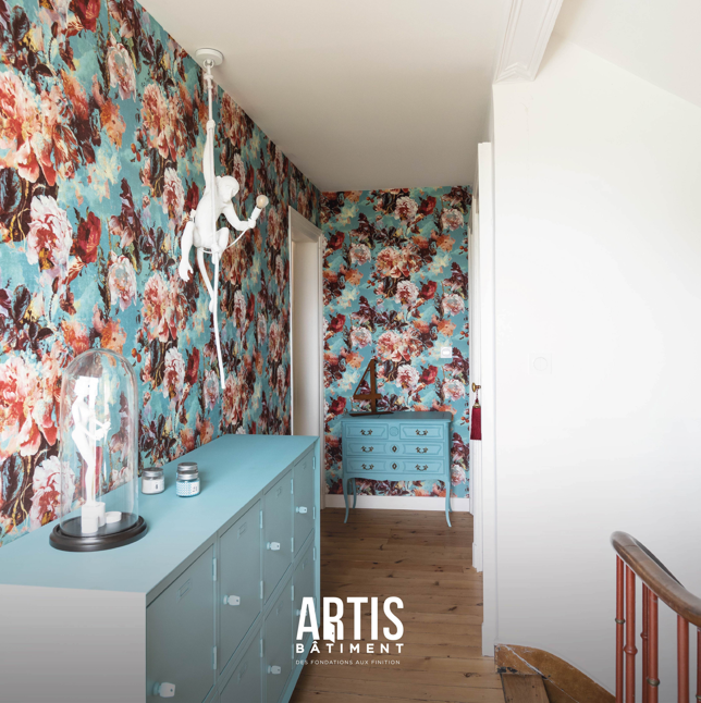 Couloir décoré avec papier peint floral et mobilier bleu dans une maison rénovée.