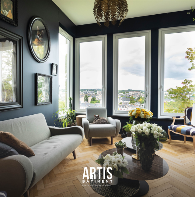 Salon lumineux rénové avec grandes fenêtres et vue dégagée sur la ville.