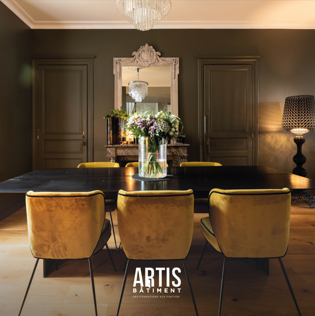 Salle à manger élégante avec table noire, chaises velours et cheminée décorative.