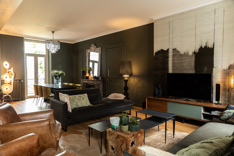 Salon et salle à manger rénovés dans une maison ancienne avec parquet bois, mobilier contemporain et grande fenêtre.