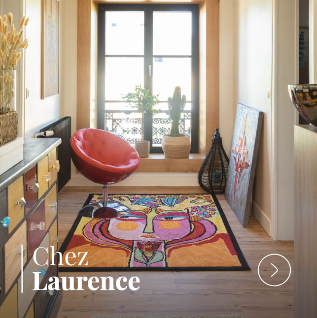 Entrée de maison décorée avec fauteuil rouge, tapis artistique coloré et grande fenêtre.