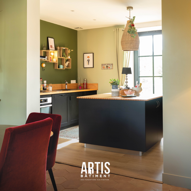 Cuisine ouverte avec îlot central bois et meubles noirs dans une maison rénovée.