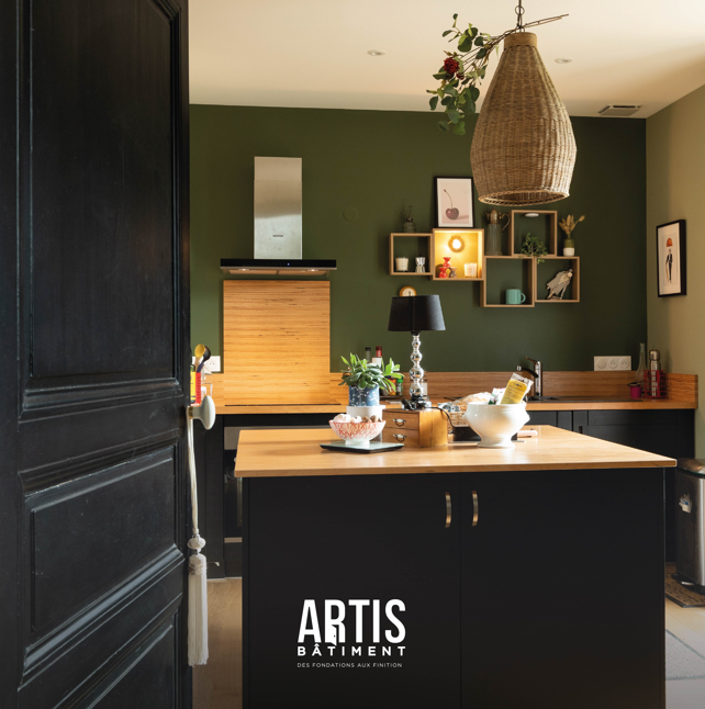 Cuisine moderne avec mur vert, meubles noirs et plan de travail bois.