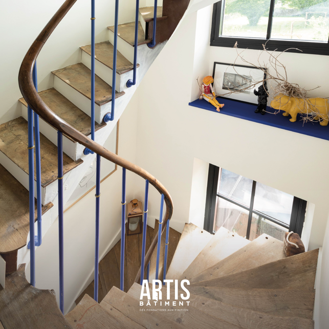 Escalier en bois d’une maison ancienne avec garde-corps bleu et paliers lumineux.