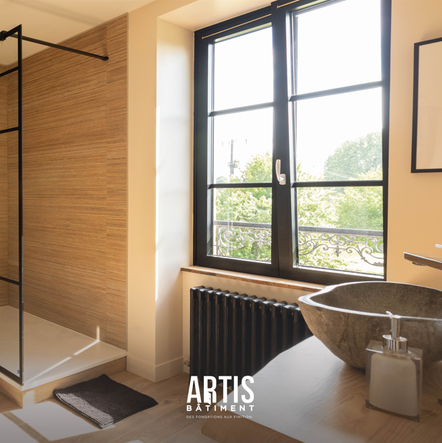Salle de bain moderne avec douche vitrée, vasque en pierre et grande fenêtre.