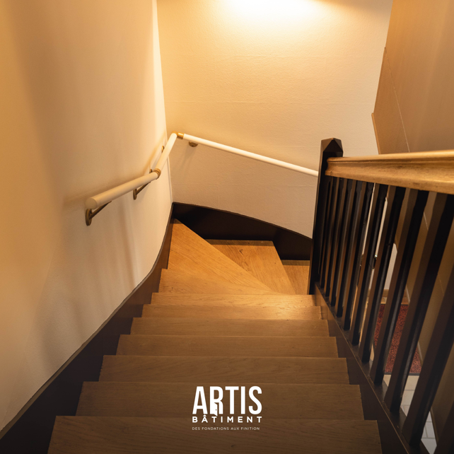 Escalier en bois rénové avec garde-corps noir dans une maison.