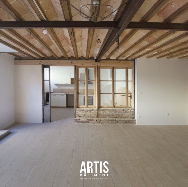 Salon rénové avec sol effet bois, poutres apparentes et mur en briques anciennes.