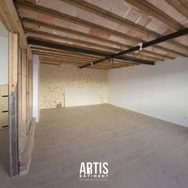 Grande pièce rénovée avec plafond vouté apparent et sol effet bois après travaux de plâtrerie.