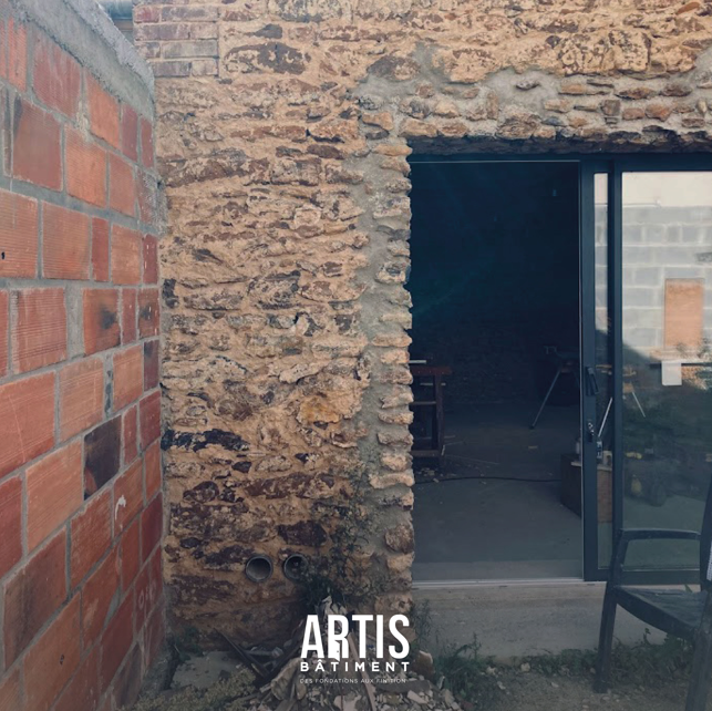 Ouverture en façade avant rénovation avec mur en pierre brute et aménagement extérieur en cours.