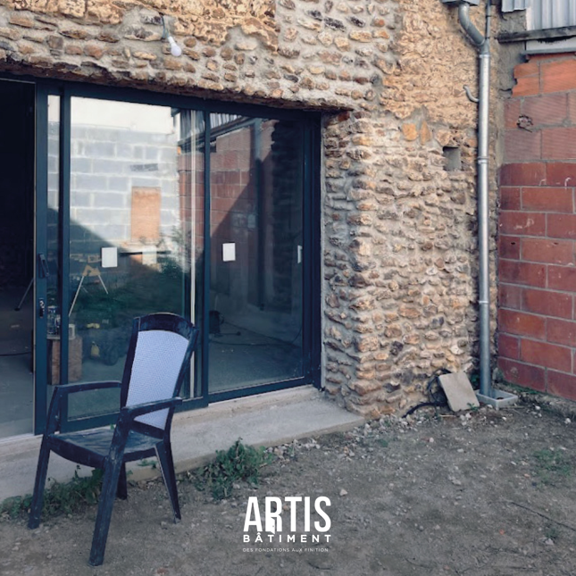 Façade en pierre avec baie vitrée avant finitions d’enduit et aménagement extérieur.