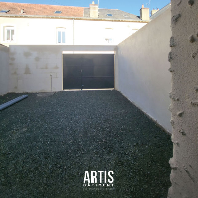 Cour extérieure rénovée avec revêtement en gravier et portail noir en fond de parcelle.