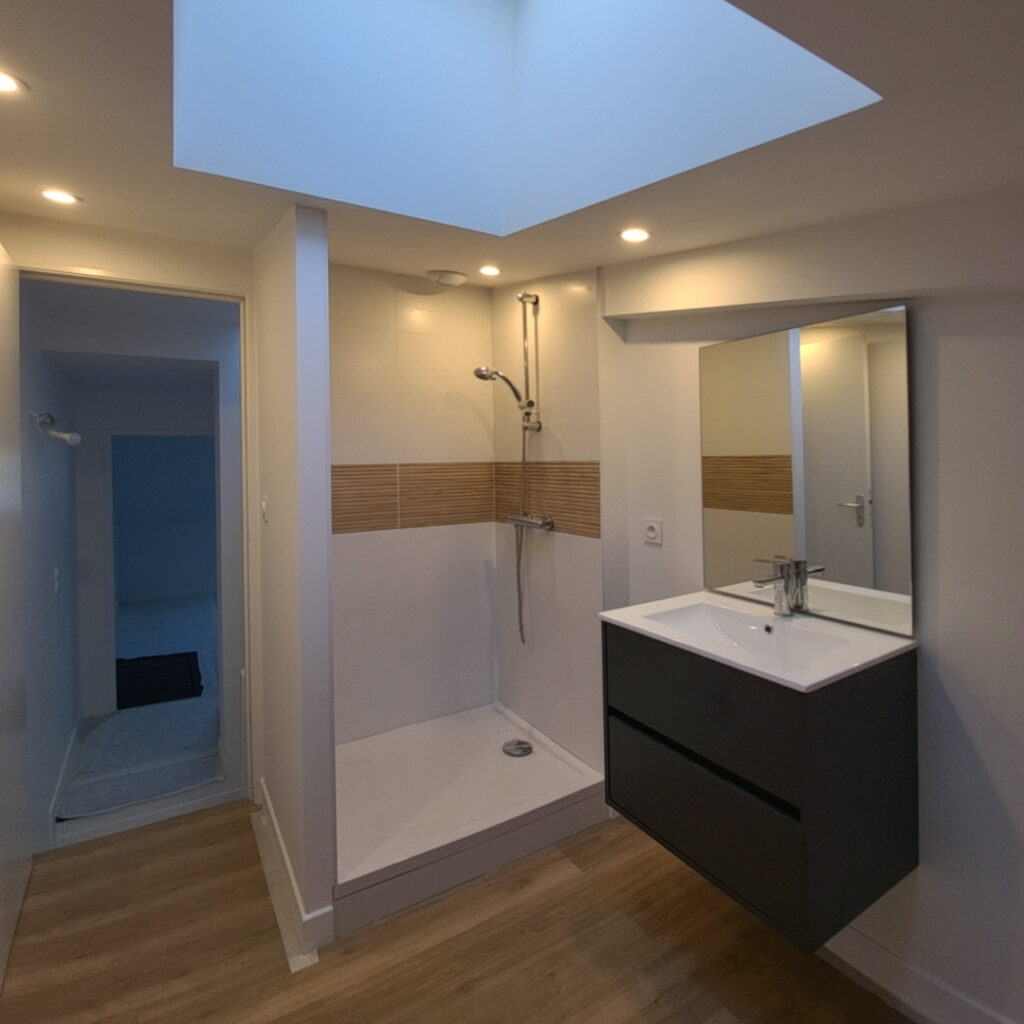 Salle de bain rénovée avec douche, meuble vasque suspendu et puits de lumière au Mans.