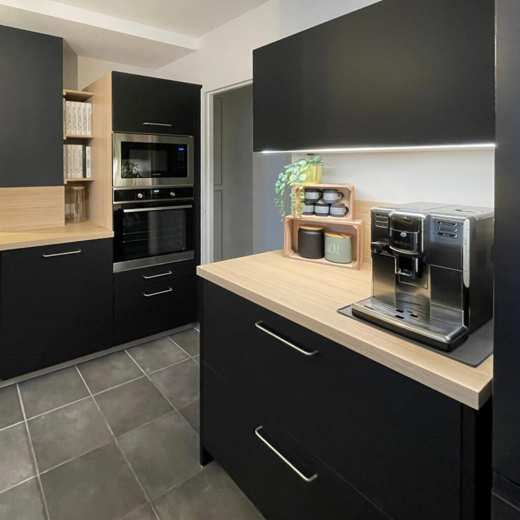 Cuisine rénovée moderne avec meubles noirs, plan de travail bois et électroménager intégré.